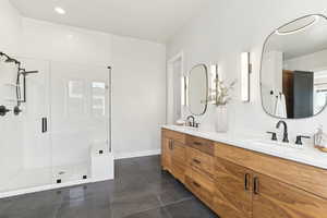 Bathroom with tile patterned floors, double vanity, a stall shower, and a sink