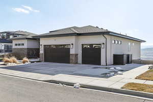 View of front of home with a shingled roof, a garage, stone siding, and stucco siding