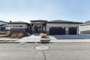 Prairie-style home featuring stucco siding, stone siding, concrete driveway, and an attached garage