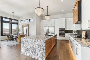 Kitchen with backsplash, a notable chandelier, stainless steel appliances, wall chimney exhaust hood, and a sink