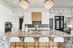 Kitchen featuring a notable chandelier, a sink, decorative backsplash, and stainless steel double oven