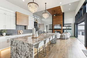 Kitchen with light wood-type flooring, backsplash, a large island with sink, and white cabinets