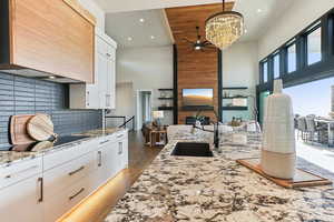 Kitchen with a notable chandelier, light wood-style flooring, a sink, black electric cooktop, and custom exhaust hood