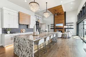 Kitchen featuring a spacious island, tasteful backsplash, wood finished floors, white cabinetry, and a fireplace