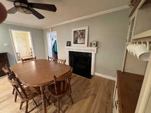 Dining space featuring a lovely fireplace for cozy ambiance ceiling fan, crown molding, solid hardwood floors