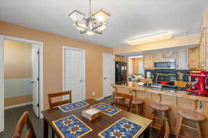 Dining room with a textured ceiling, dark tile patterned floors, baseboards, and an inviting chandelier