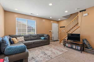 Carpeted living area featuring visible vents, baseboards, stairway, a textured ceiling, and recessed lighting