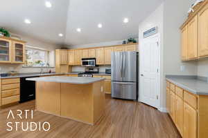 Kitchen featuring glass insert cabinets, light brown cabinets, appliances with stainless steel finishes, and a kitchen island