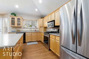 Kitchen with a sink, glass insert cabinets, light brown cabinets, and stainless steel appliances