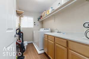 Laundry area with light wood finished floors, baseboards, laundry area, washer and dryer, and a sink