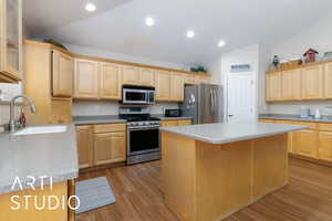 Kitchen featuring a sink, vaulted ceiling, light brown cabinetry, and stainless steel appliances