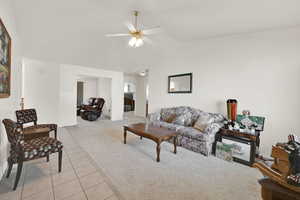 Living area with light tile patterned floors, ceiling fan, light carpet, and lofted ceiling