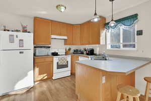 Kitchen with under cabinet range hood, light countertops, a peninsula, white appliances, and a sink