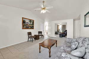 Living area with light carpet, lofted ceiling, light tile patterned floors, baseboards, and ceiling fan