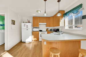 Kitchen featuring light wood-type flooring, under cabinet range hood, a sink, white appliances, and a peninsula