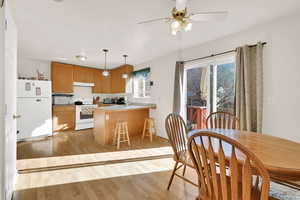 Kitchen featuring under cabinet range hood, light wood-type flooring, a peninsula, white appliances, and a sink