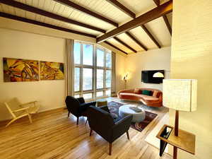 Living room with brick wall, light wood-style flooring, and vaulted ceiling with beams