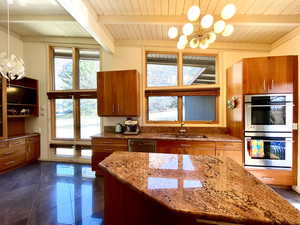 Kitchen featuring light stone countertops, a chandelier, brown cabinetry, stainless steel appliances, and a sink