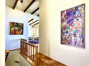 Corridor featuring an upstairs landing, beamed ceiling, brick wall, and an inviting chandelier