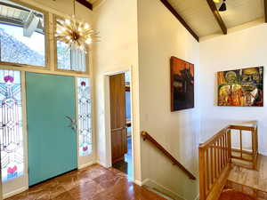 Entrance foyer with beamed ceiling, high vaulted ceiling, marble finish floor, baseboards, and a chandelier