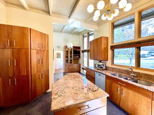 Kitchen featuring beamed ceiling, a sink, light stone counters, a center island, and dishwasher