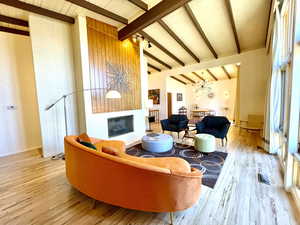 Living room with visible vents, a large fireplace, beamed ceiling, wood finished floors, and high vaulted ceiling