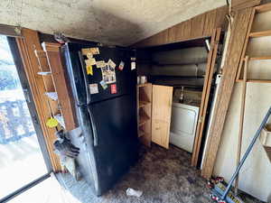 Kitchen with wooden walls, lofted ceiling, washer / dryer, freestanding refrigerator, and a textured ceiling