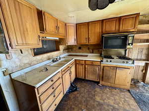 Kitchen with black microwave, light countertops, brown cabinetry, gas cooktop, and a sink