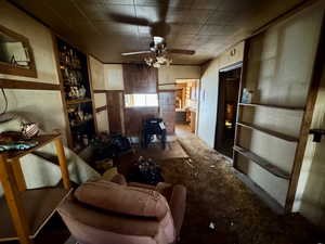 Living room with built in shelves, wood walls, and ceiling fan