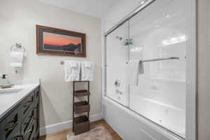 Bathroom with vanity, wood finished floors, combined bath / shower with glass door, and baseboards