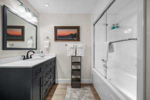 Bathroom featuring combined bath / shower with glass door, baseboards, wood finished floors, and vanity