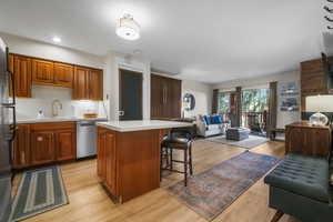 Kitchen with a kitchen bar, a sink, open floor plan, light countertops, and dishwasher