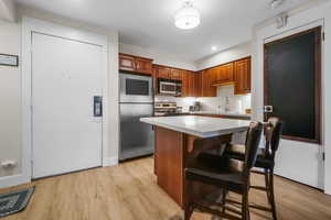 Kitchen with stainless steel appliances, a kitchen bar, a kitchen island, and light wood finished floors