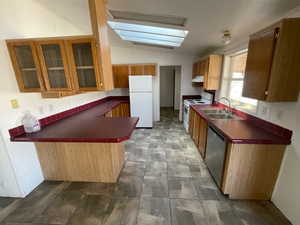 Kitchen featuring a sink, white appliances, glass insert cabinets, a peninsula, and lofted ceiling