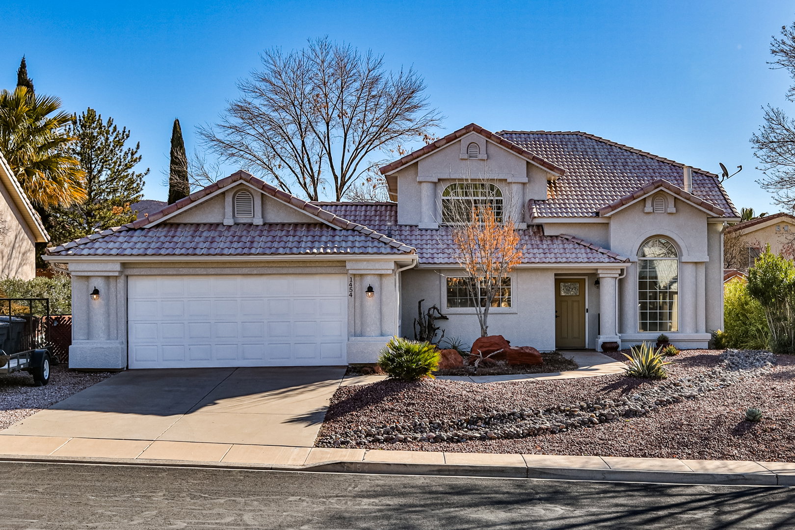 View of front facade featuring a tiled roof, an attached garage, driveway, and stucco siding