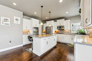 Kitchen with a kitchen island, appliances with stainless steel finishes, dark wood-style flooring, and white cabinetry