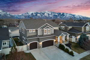 View of front of home with fence, roof with shingles, a garage, stone siding, and a mountain view