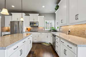 Kitchen featuring a sink, backsplash, a kitchen island, dark wood-style floors, and appliances with stainless steel finishes