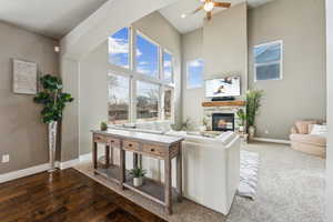 Living room with wood finished floors, baseboards, a fireplace, ceiling fan, and a towering ceiling