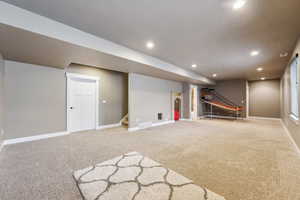 Finished below grade area featuring visible vents, carpet floors, baseboards, recessed lighting, and stairs