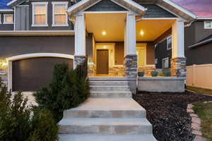 Exterior entry at dusk featuring stone siding, stucco siding, and a porch