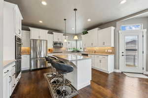 Kitchen featuring a kitchen island, dark wood finished floors, hanging light fixtures, white cabinets, and stainless steel appliances