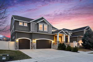 Craftsman-style home featuring a gate, fence, driveway, stone siding, and a garage