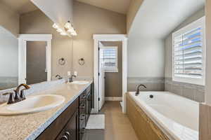 Full bath with double vanity, a garden tub, lofted ceiling, and a sink