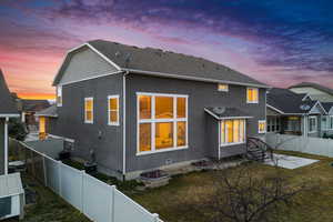 Back of property at dusk with a yard, a fenced backyard, roof with shingles, and stucco siding