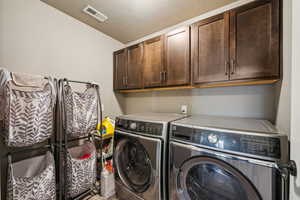 Clothes washing area featuring cabinet space, visible vents, independent washer and dryer, and a textured ceiling