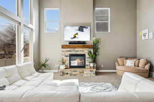 Carpeted living room with a stone fireplace, a high ceiling, and baseboards