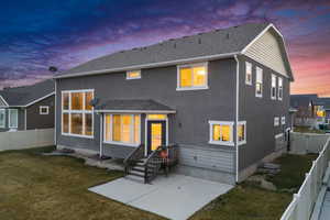 Back of property at dusk with a lawn, roof with shingles, and a fenced backyard