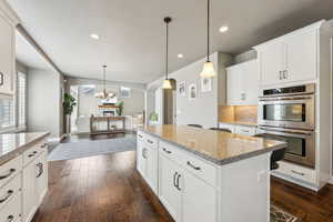 Kitchen with a kitchen island, light stone countertops, pendant lighting, stainless steel double oven, and dark wood-style flooring