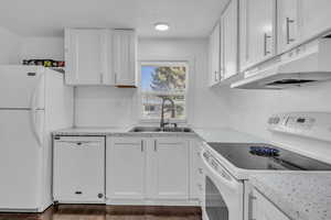 Kitchen with white appliances, dark wood finished floors, a sink, white cabinets, and under cabinet range hood